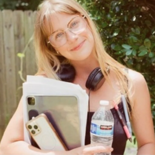 Picture of Madeline Ramsey holding water bottle, phone, laptop with headphones around her neck.