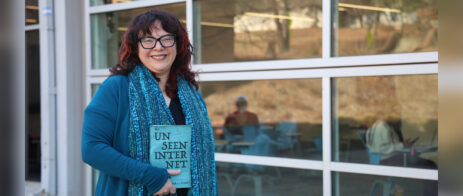 Shira Chess holds a book, "The Unseen Internet," as she poses for a picture in front of Grady College.