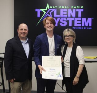 Brooks Thomason stands alongside one man and one woman, receiving an award from the National Radio Talent System.