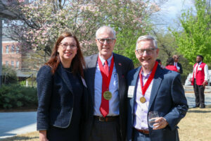 Two men and a woman pose for a picture outside. The men are each wearing a Grady Fellowship medal.