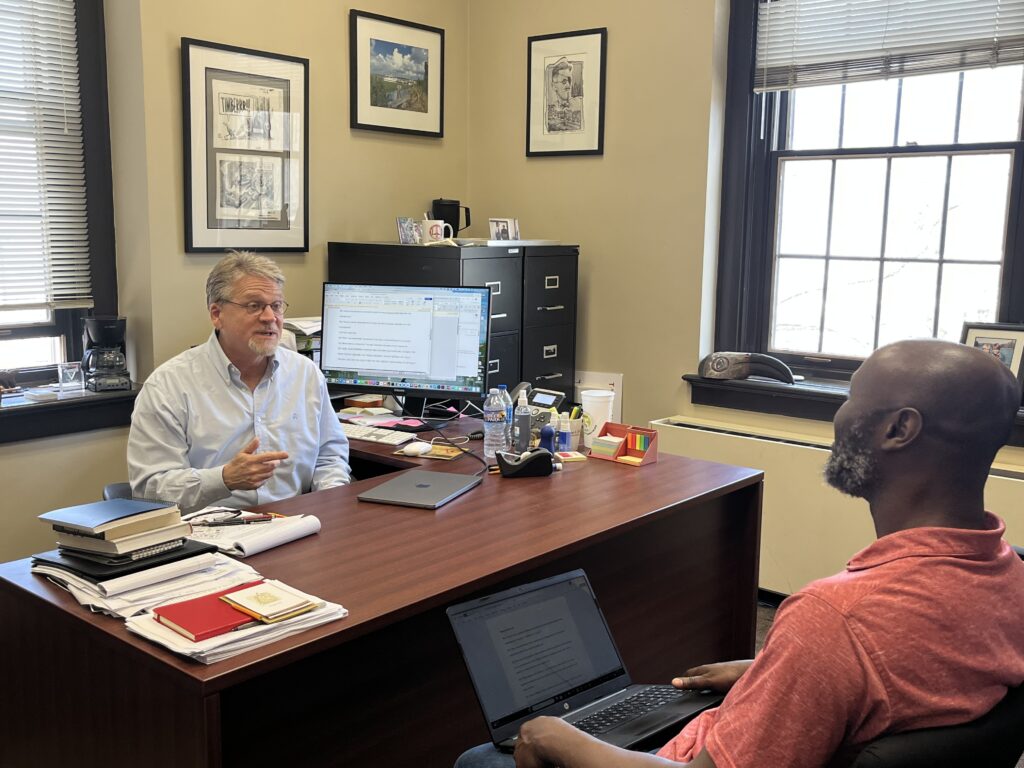 Wilson Lowrey is pictured at his desk meeting with a Ph.D. student at the University of Alabama.
