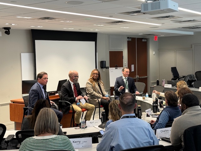 Four people sit in front of a room and host a panel discussion.