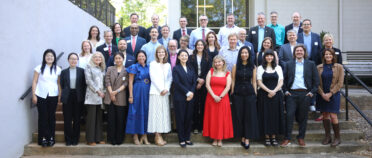 A large professional group photo of approximately 40 participants of the Crisis Communication Think Tank (CCTT) 2026 meeting. They are posed outdoors on concrete stairs in front of a modern building with large glass windows.