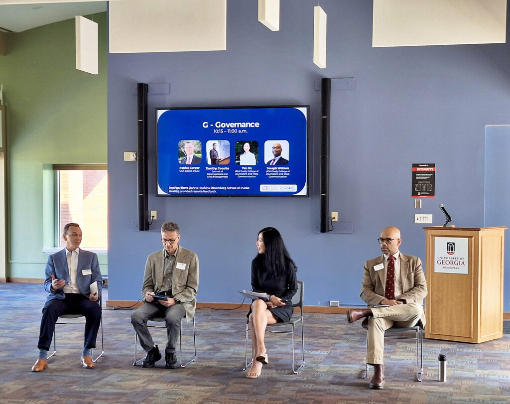 A panel of four people sit in front of a digital sign that reads G-Governance.