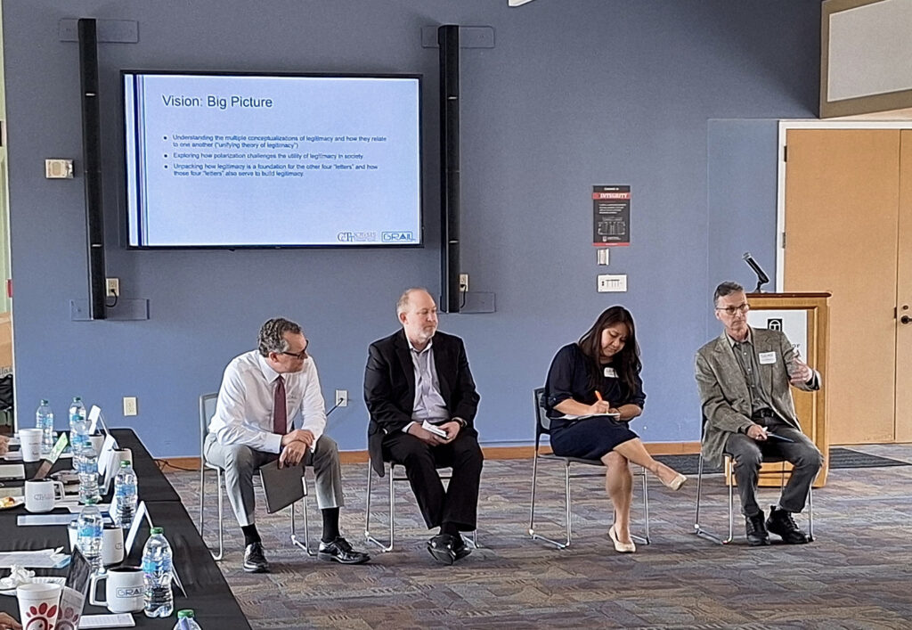 A panel of four people sit and present in front of a digital screen with the headline Vision: Big Picture.