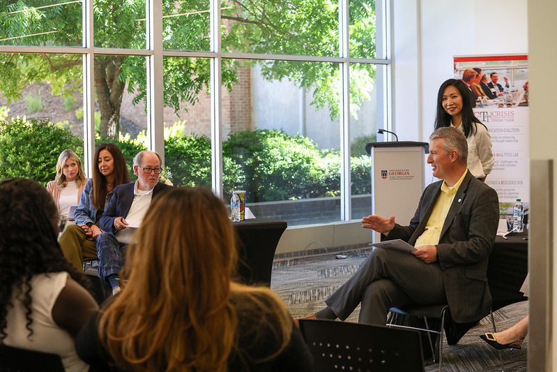 A panel of industry professionals are seated talking with students as Yan Jin stands and looks on.