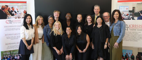Industry professionals and students pose for a picture in front of a black screen. Two CCTT Crisis Communication Think Tank banners are at their sides.