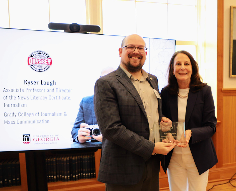 Kyser Lough and Marisa Anne Pagnattaro pose for a picture with an award. In the background is a picture of Lough and the FYO logo.