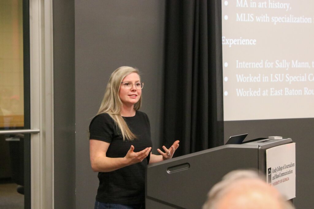 A woman stands behind a podium with a presentation projected on the wall behind her.