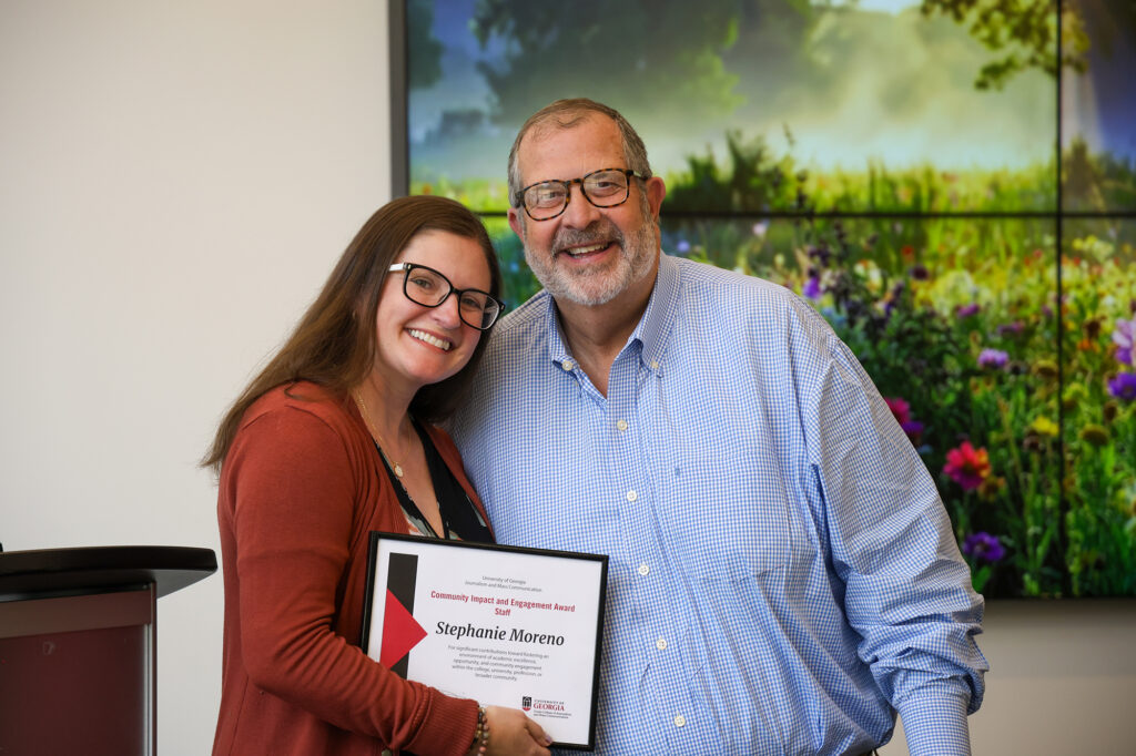 Stephanie Moreno leans her head toward Dean Davis and smiles while she displays her certificate for the Community Impact and Engagement Award.