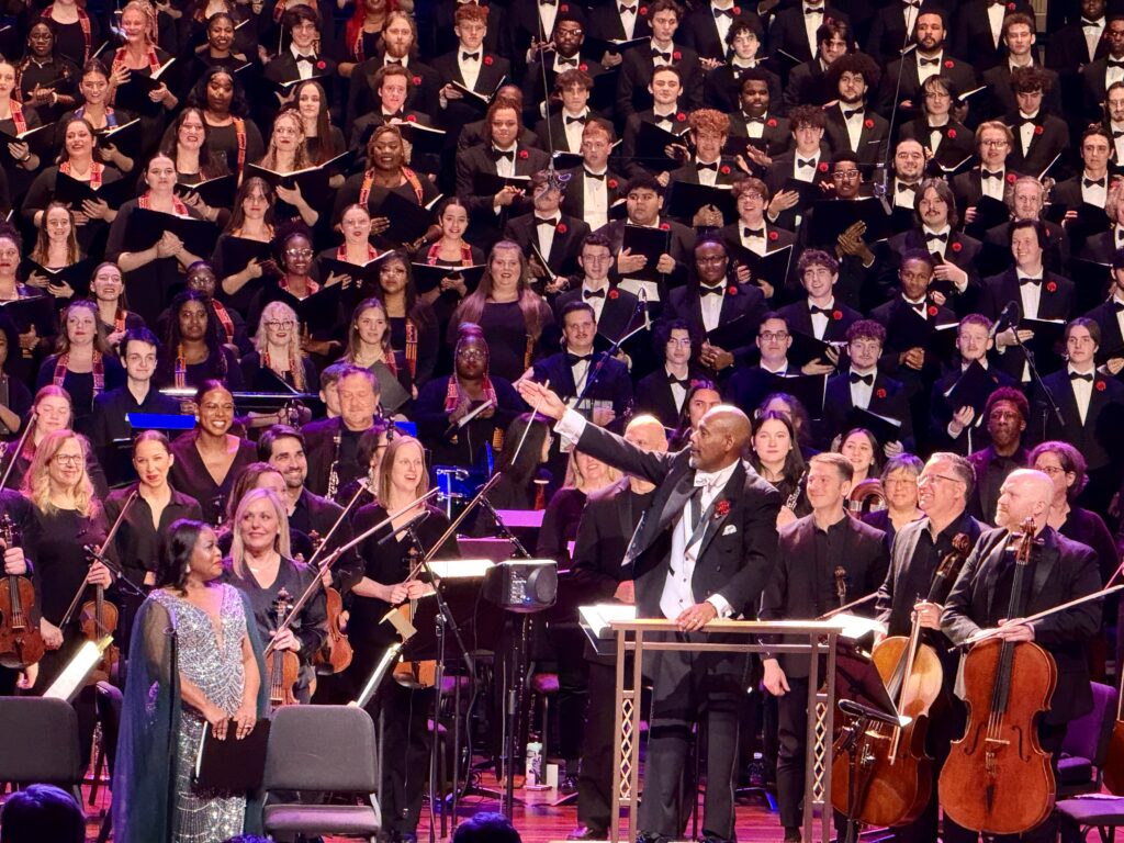 A man stands in front of a large crowd of choral, orchestral and band members performing in "Requiem for Colour."