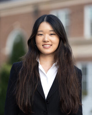 A young woman poses for a headshot with a brick building in the background.