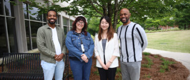 Four faculty pose for a picture in front of Grady College.