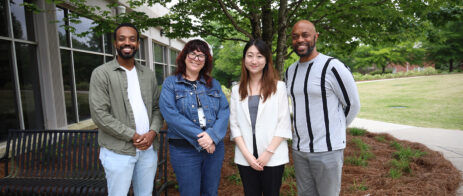 Four faculty pose for a picture in front of Grady College.