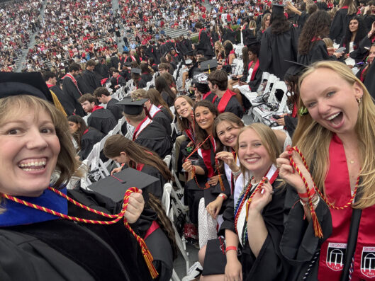 Several students and a faculty member who off their cords in a large graduation crowd.