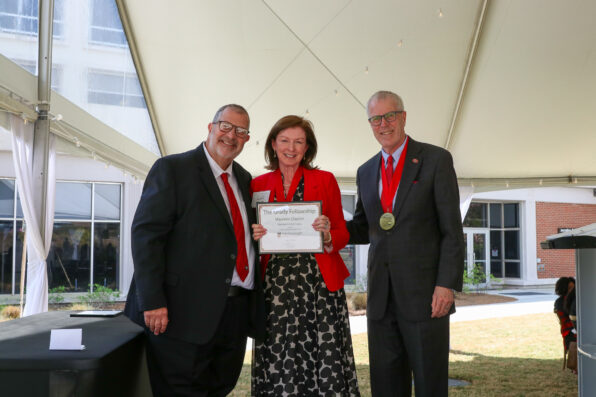 Maureen Clayton holds a Grady Fellowship certificate and poses for a picture between two men.
