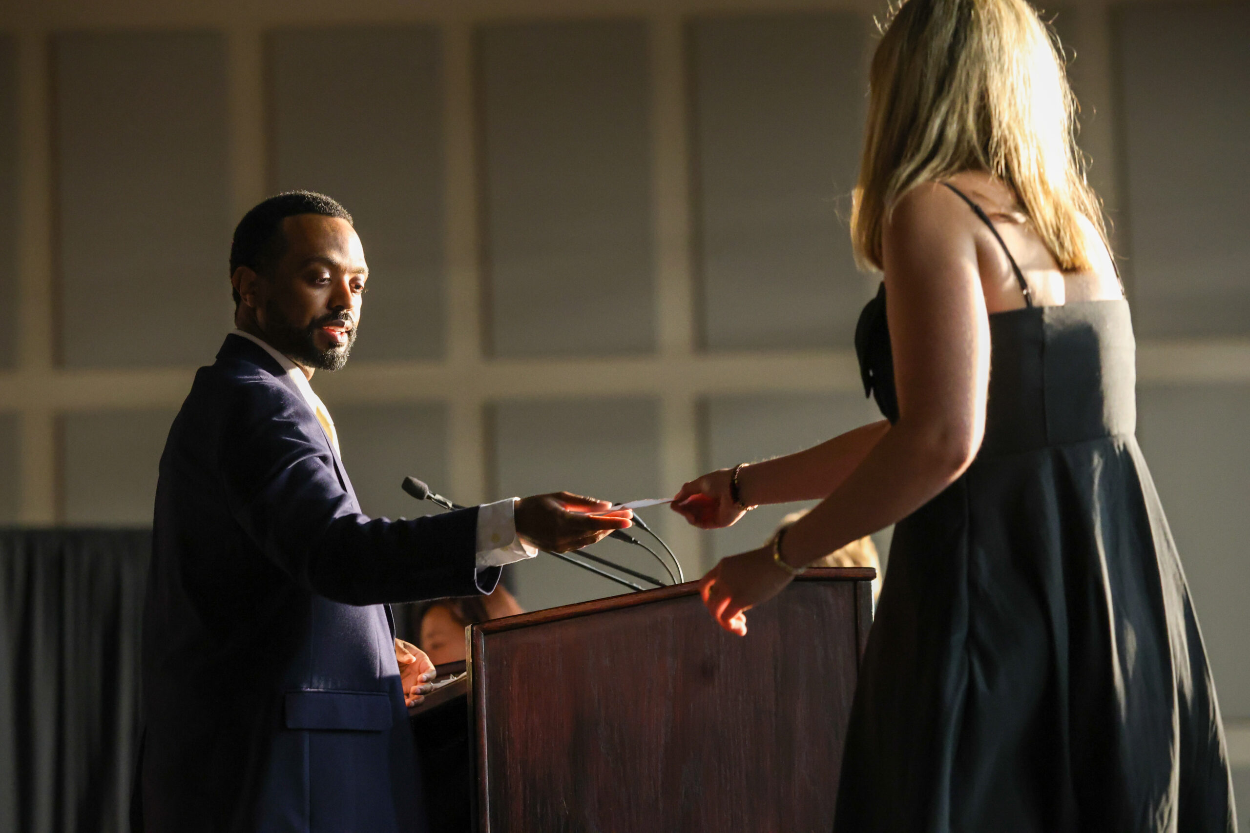 A man standing behind a podium receives something from a blonde young woman.