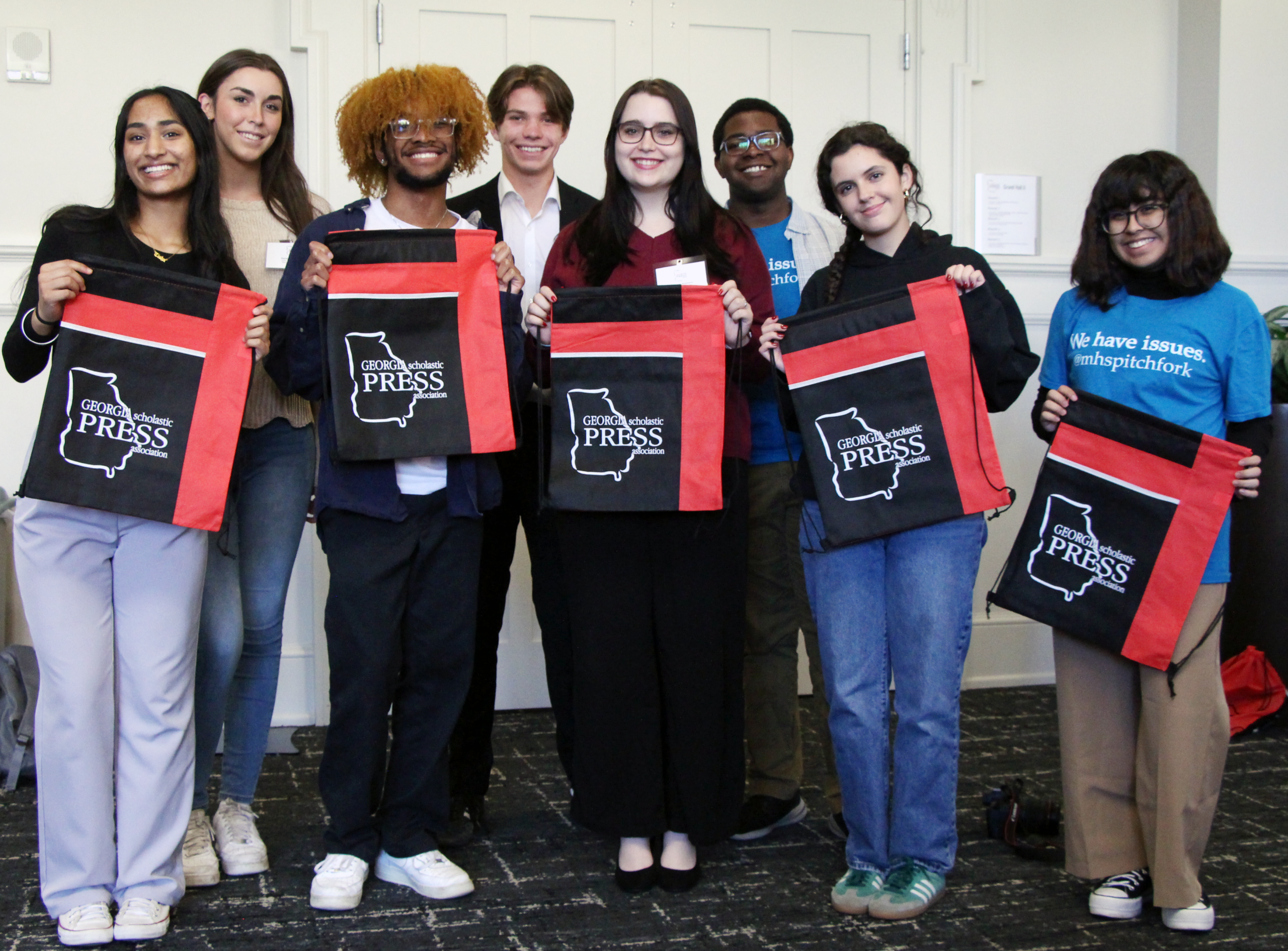Eight students stand to pose for a picture holding tote bags that read "Georgia Scholastic Press Association."