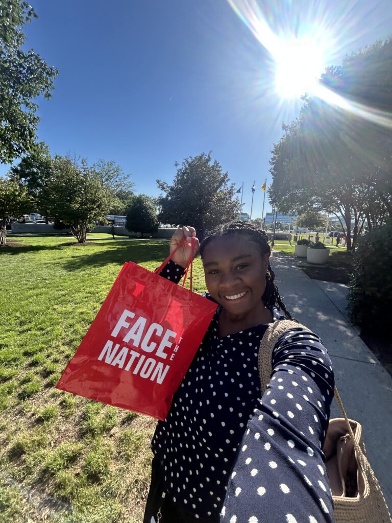 Courtney Craft smiles outside with a red CBS Face the Nation bag.