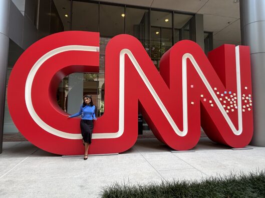 Full-body picture of Sanjana Copu standing in front of a CNN sign at an office building.