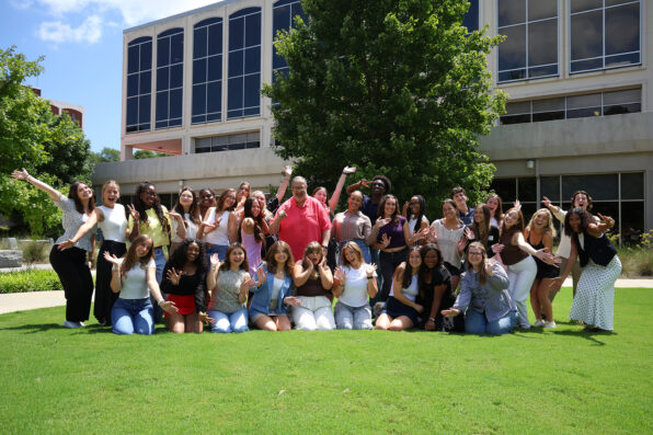 Dean Davis and a large group of students make funny faces while posing for a picture in the lawn in front of Grady College.