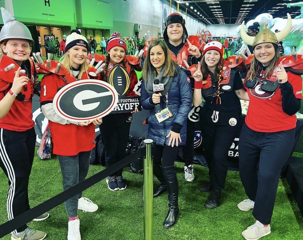 A group of University of Georgia Bulldog fans pose in room lit green on a astroturfing. 