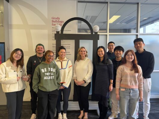 A group of students and faculty pose for a picture with a replica of the UGA Arch in the background.