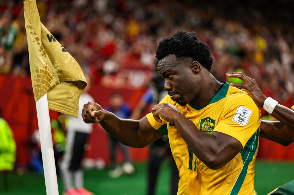 A soccer player in a yellow jersey from the Australia team playfully spars with a soccer flag.