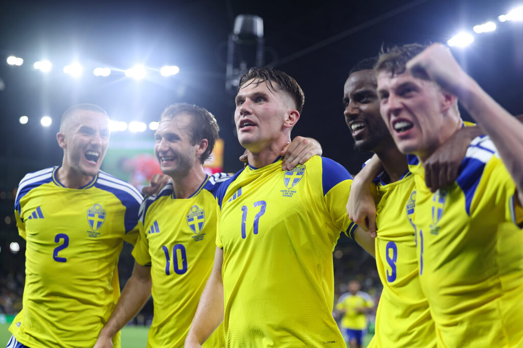 Five male soccer players in yellow jerseys with arms around one another celebrate.