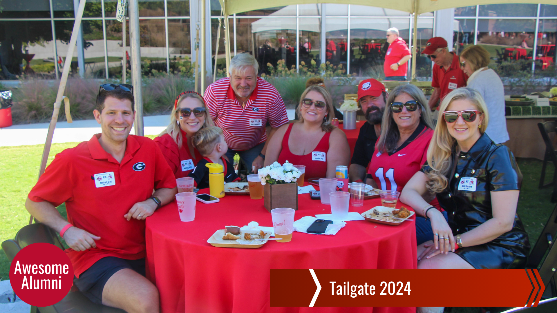 Group of people gather around an outside table with food.