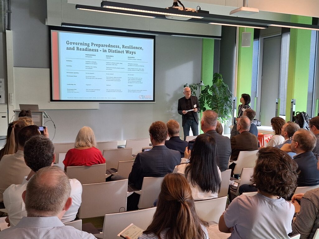 A man presents a slide to a group of people. The title of the slide is Governing Preparedness, Resilience, and Readiness.