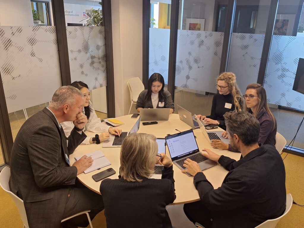 A group of people sit around a round table and work on their computers.