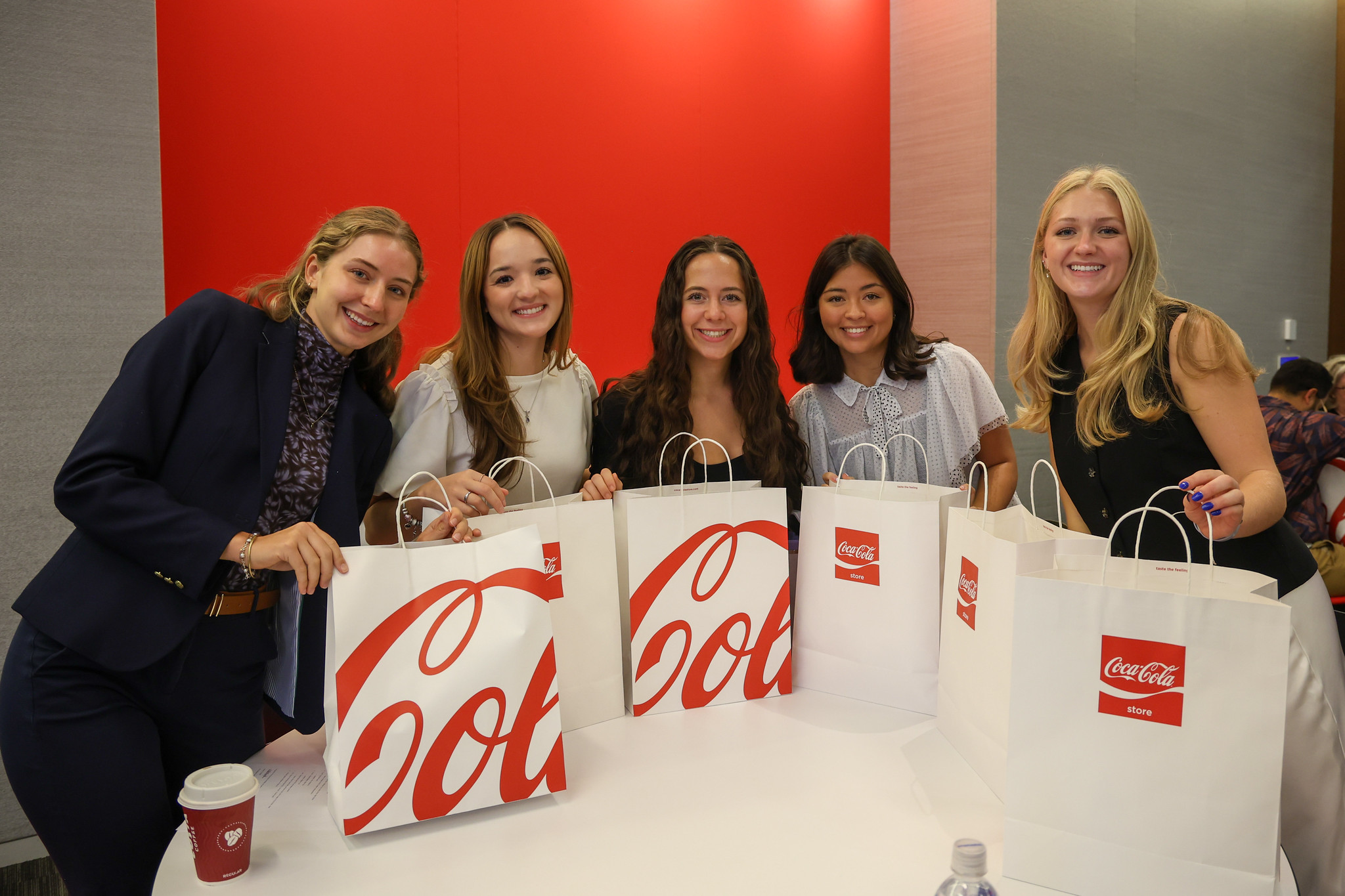 Five female students pose for a picture in back of a table with large white bags that say Coca-Cola.