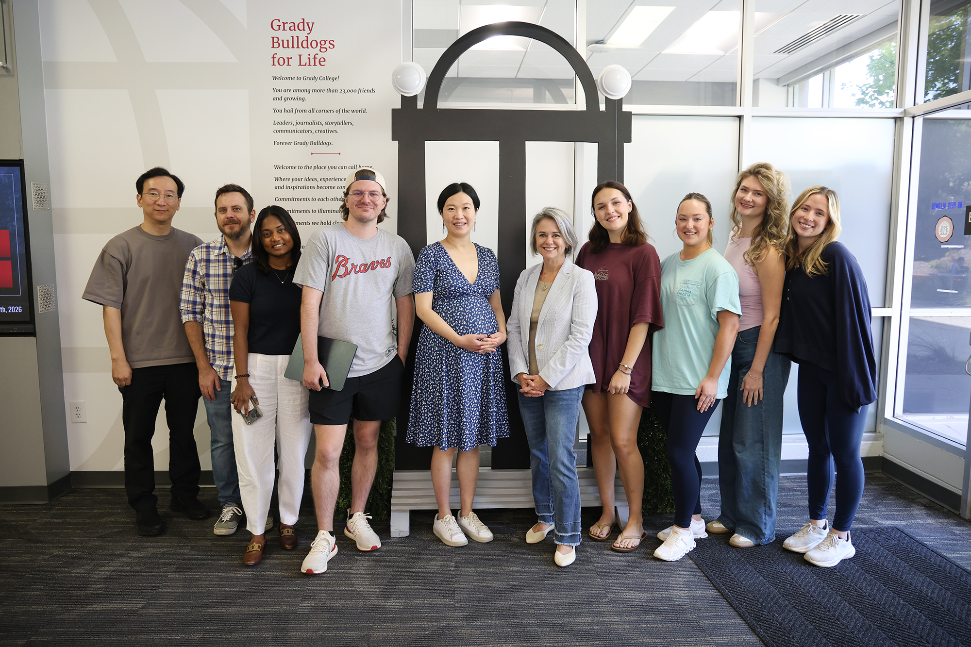 A group of professors and students pose for a picture in front of the arch replica inside Grady College.