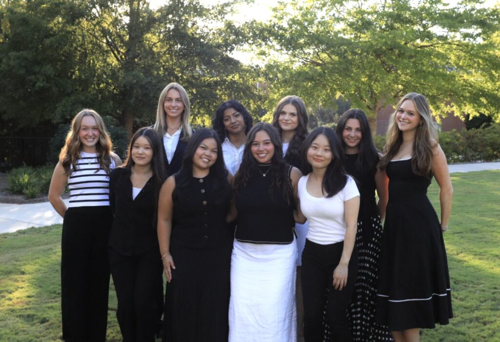 ADPR Connection 2026 Executive Team Members stand together for a picture. There are two rows of women, six women in the back and four women in the front. They are standing in front of a natural background of trees with sun shining through the trees.