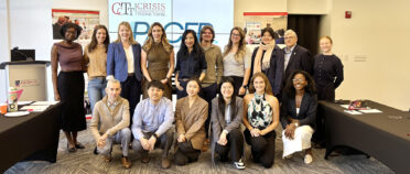 A group of students, professionals and faculty pose for a picture in front of a digital screen that has a Crisis Communication Think Tank logo.