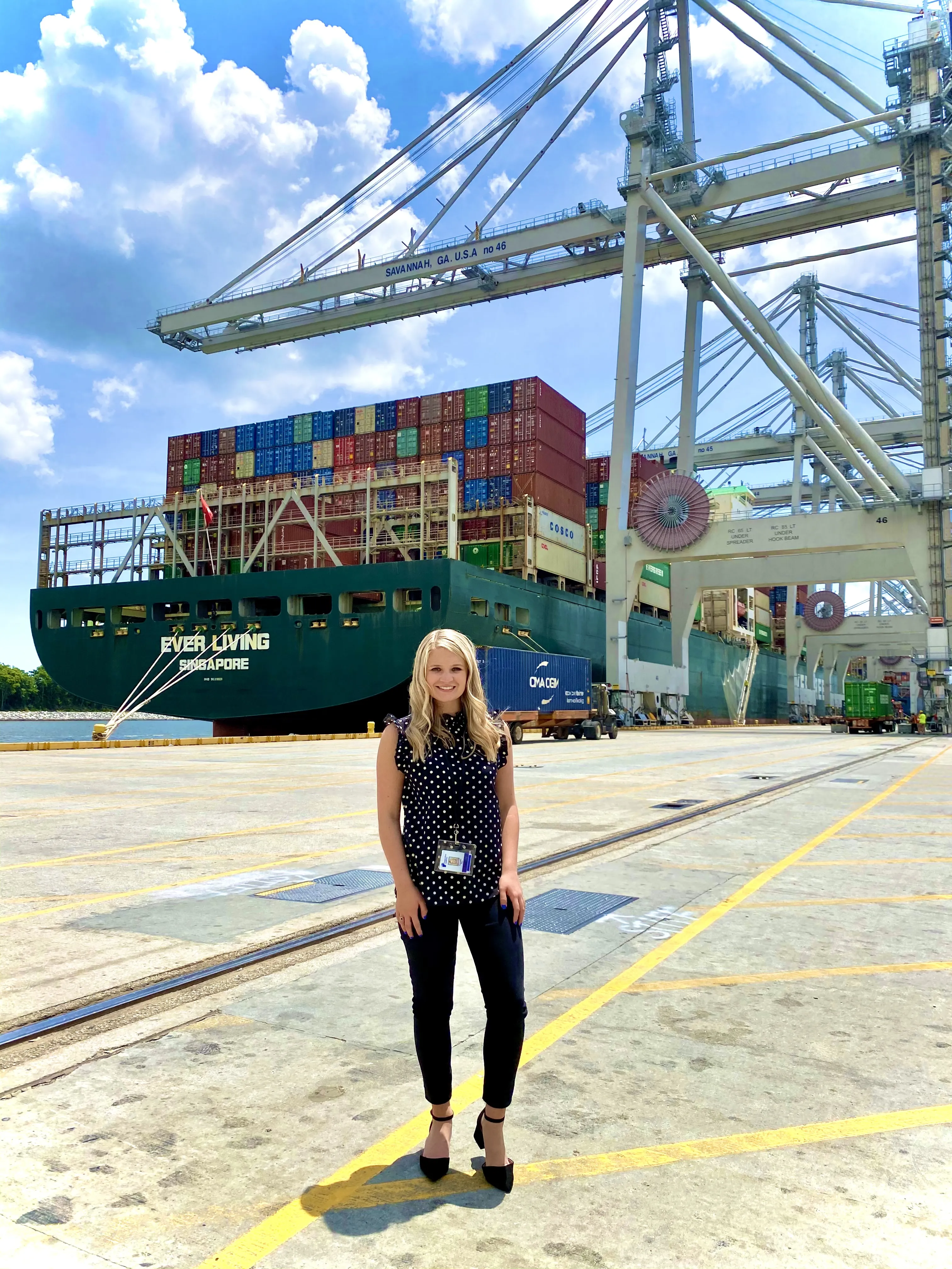 Camuso in black pants and a black blouse standing with a ship in the background