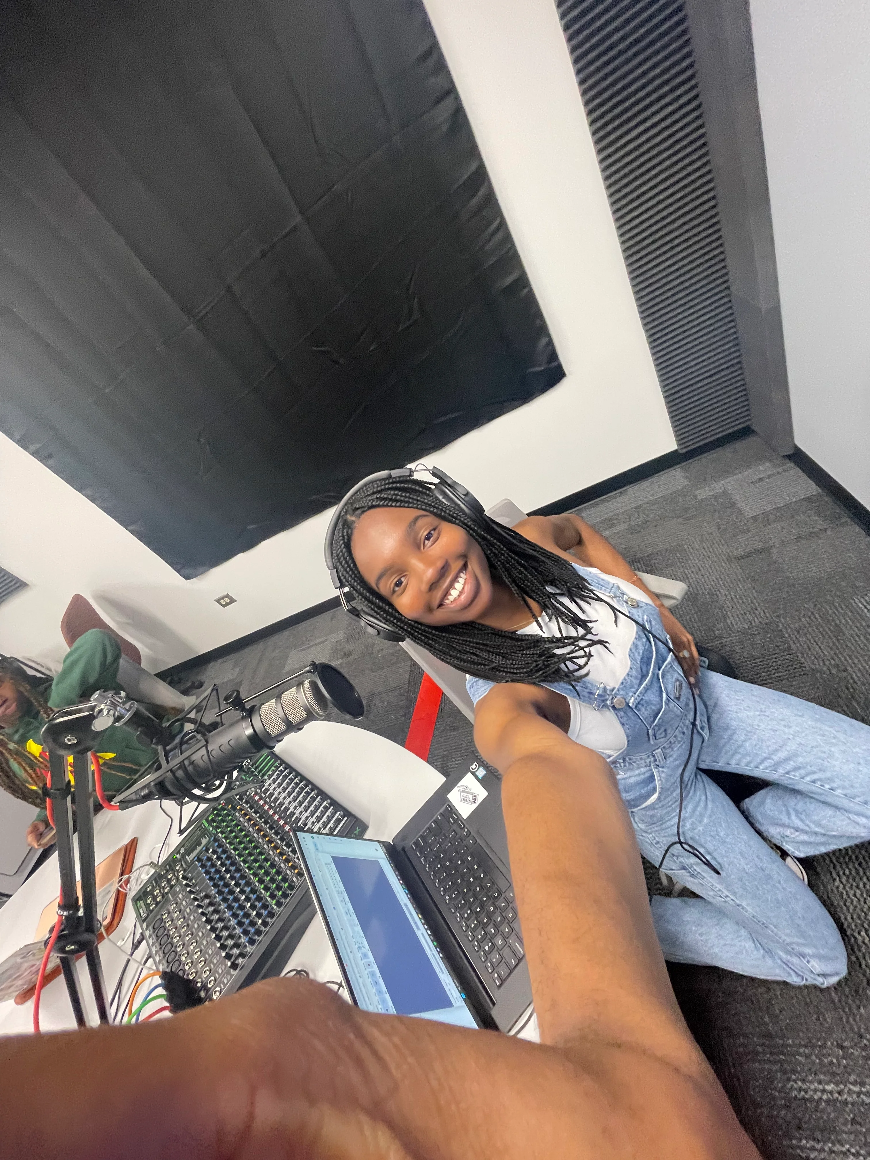 Chiamaka Uwagerikpe sitting in a chair in a podcast studio holding up her phone to take a selfie.