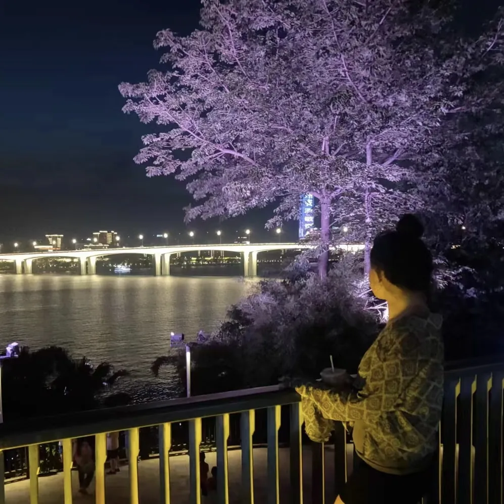 Photo of a bridge and a tree lit up with purple lights and the back of a person looking at the bridge.