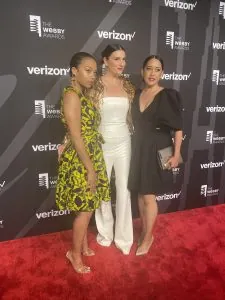 Chappell (middle) at the Webby Awards standing on a red carpet with a step and repeat in the background. 