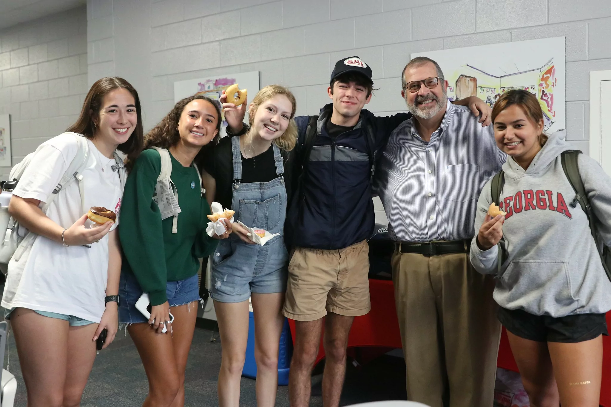 Students holding doughnuts pose with Dean Davis for a photo.