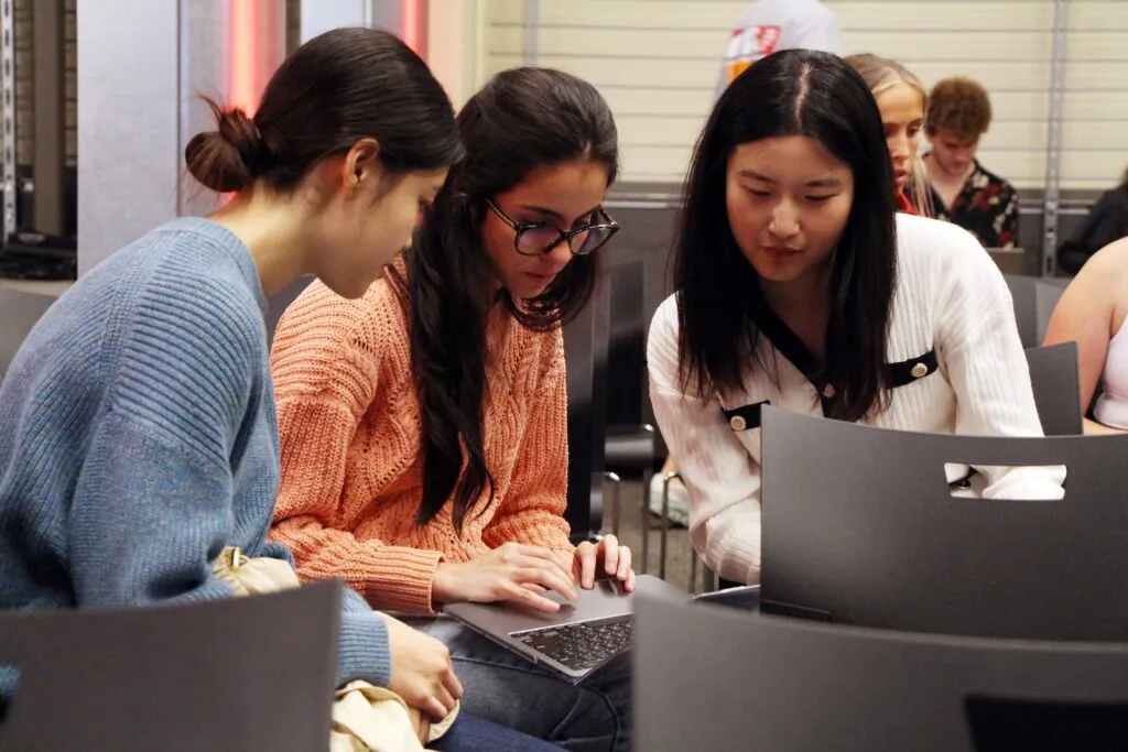 Three women look at a computer together.