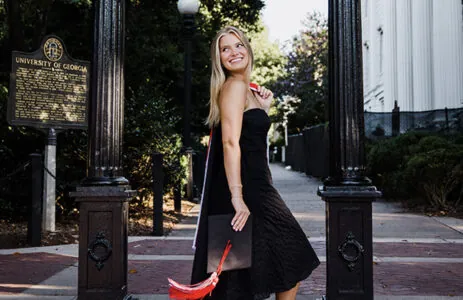 Audrie Uphues stands at the UGA Arch with a cap and gown.