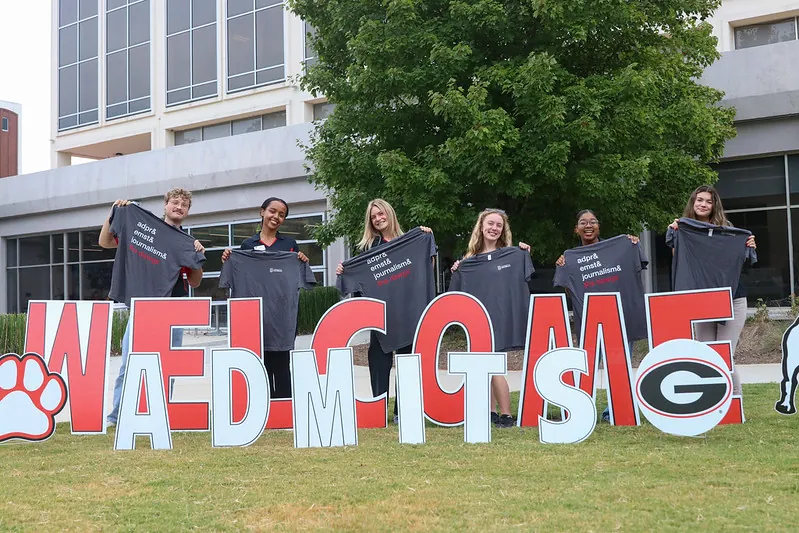 Grady College studetn ambassadors stand outside of the College behind yard letters that read "Welcome Admits."