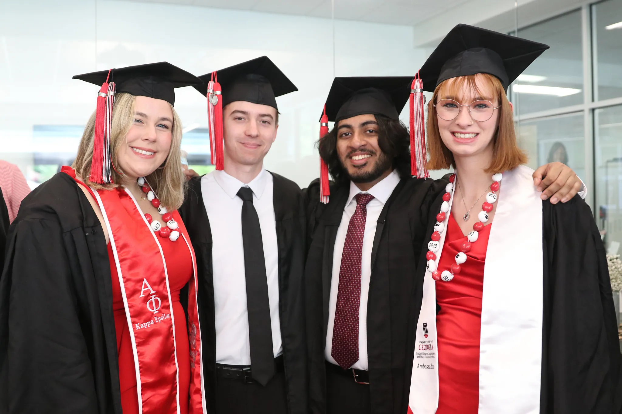 Four Grady College students pose for a photo in the PAF with graduation caps on.