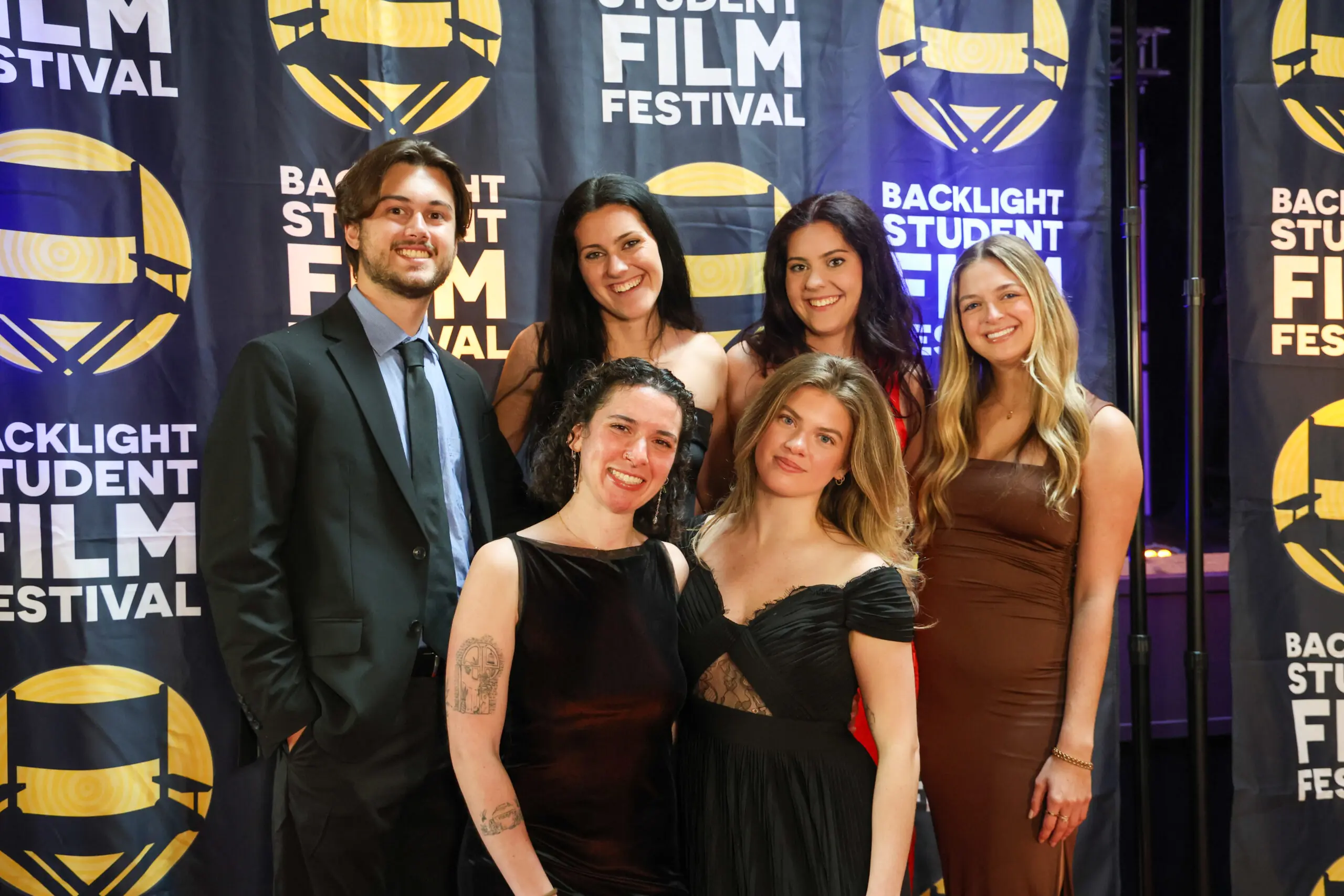 Timi Meade stands with other students in front of a Backlight Student Film Festival backdrop.