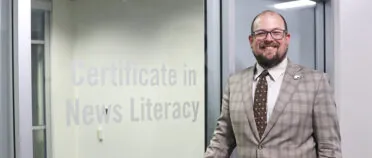 Headshot of Kyser Lough in front of a sign that reads "Certificate in News Literacy."