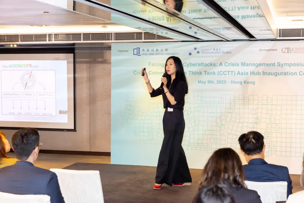 Yan Jin speaks into a microphone in front of a digital display.