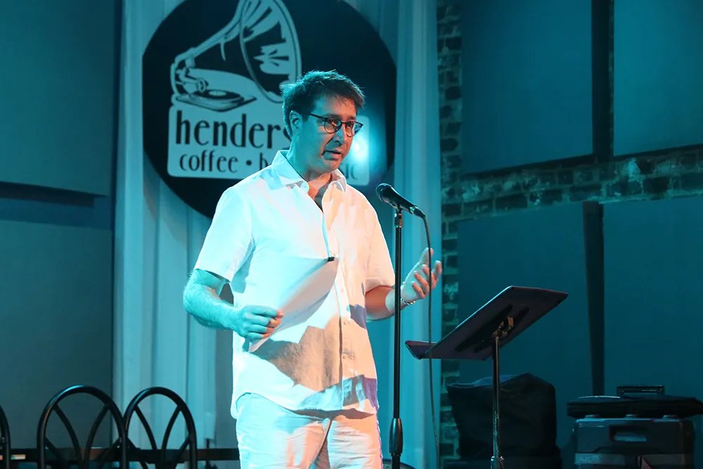 An MFA Narrative Nonfiction student reads from a paper in his hand while standing at a microphone.