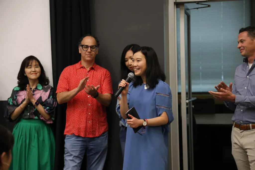Fay Chen talks into a microphone as faculty applaud behind her.